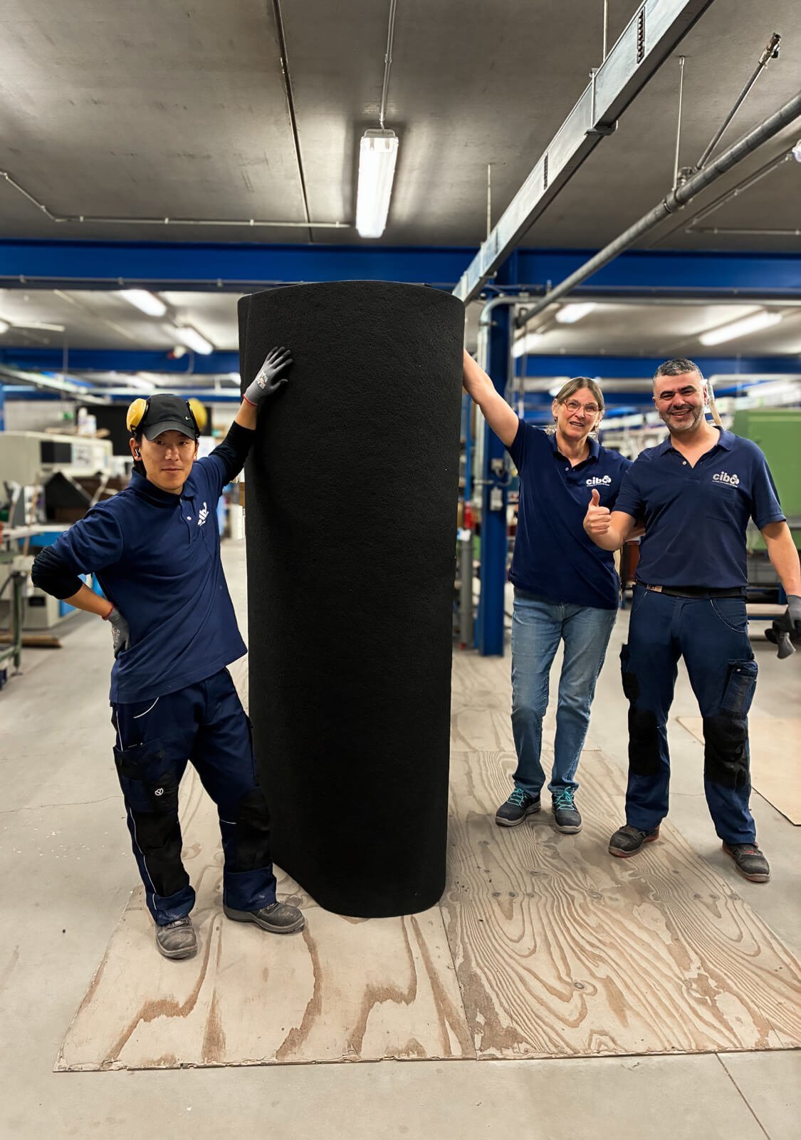 Cibo employees beside a roll of abrasive belt material in the workshop